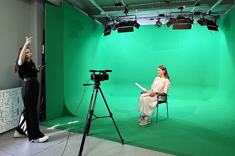 一间电影工作室，明亮的绿色幕布背景、三脚架上的摄影机和头顶的摄影灯