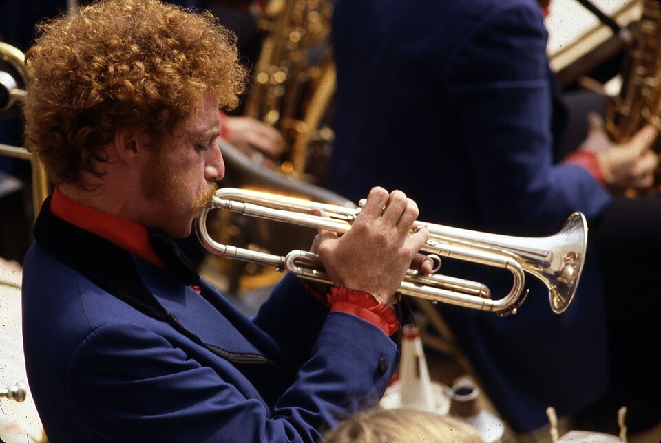 A musician playing a trumpet with saxophone players in the background