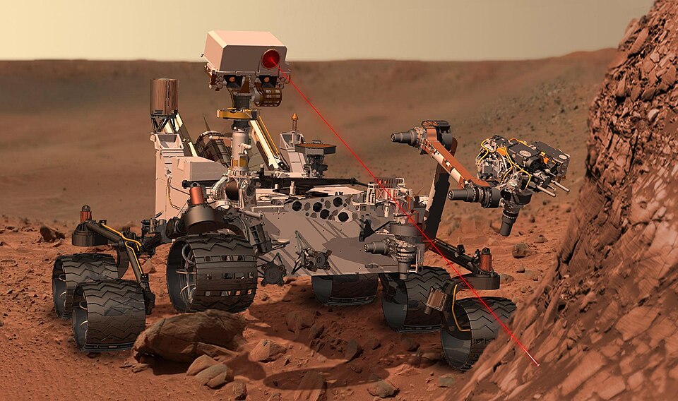 The Curiosity rover on the surface of Mars with red rocky terrain