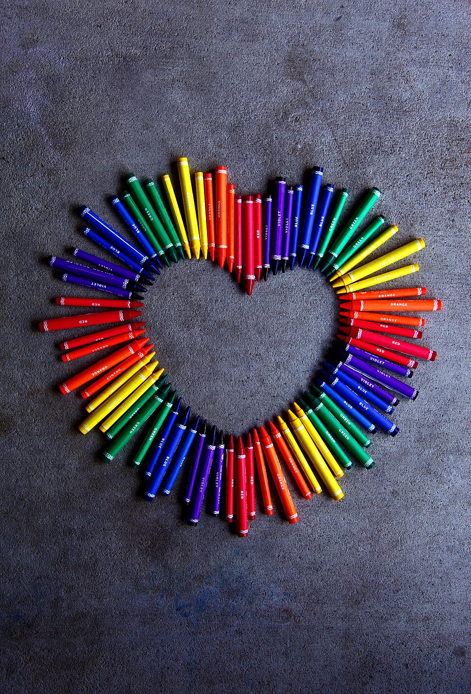 Crayones coloridos organizados en forma de corazón arcoíris