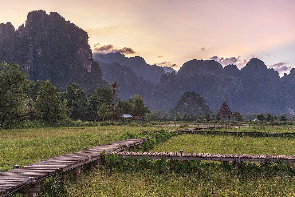 Una hermosa fotografía de paisaje de montañas al atardecer con un camino de madera que lleva a una cabaña