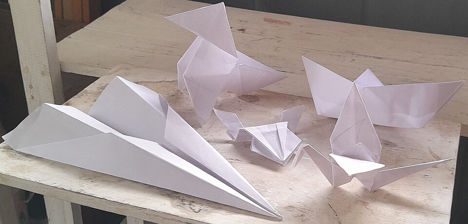 Figuras de origami tradicionales que incluyen un pájaro, barco, avión, rana saltarina y grulla hechos de papel blanco