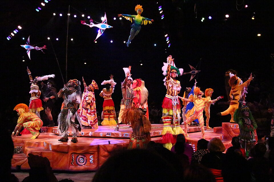 Performers in colorful animal costumes on stage during the Lion King musical