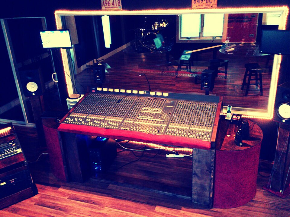 La sala de control de un estudio de grabación con una consola mezcladora y una ventana que da a la cabina de grabación