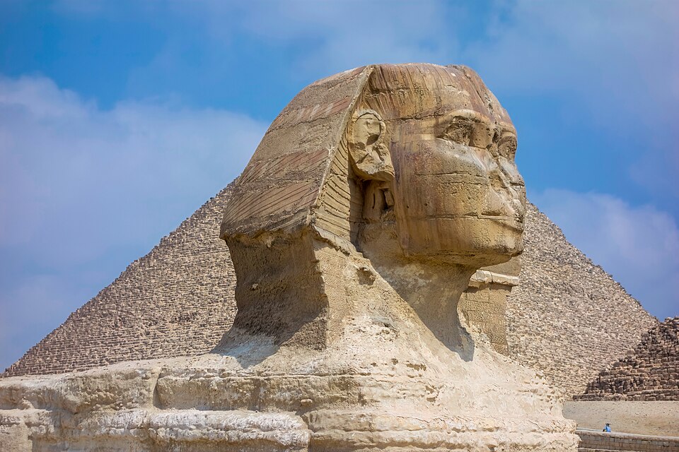 The Great Sphinx of Giza with a pyramid behind it under a blue sky